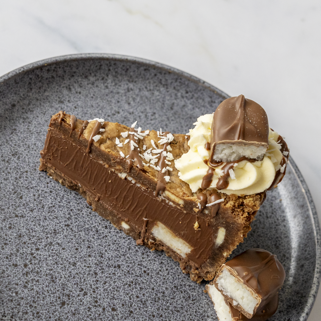 Slice of DoughGirl chocolate cake with cream and chocolate bars on a gray plate