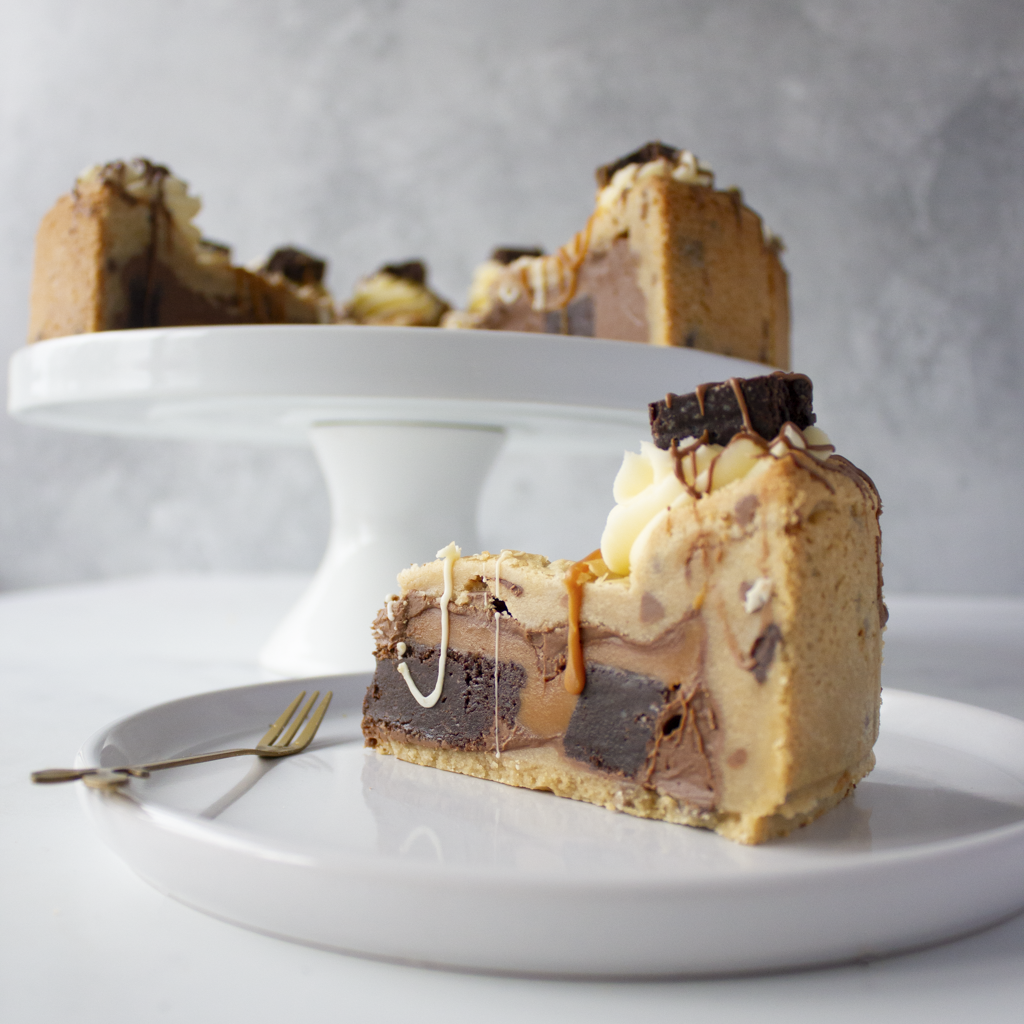 Slice of layered dessert on a white plate with a cake stand in the background.