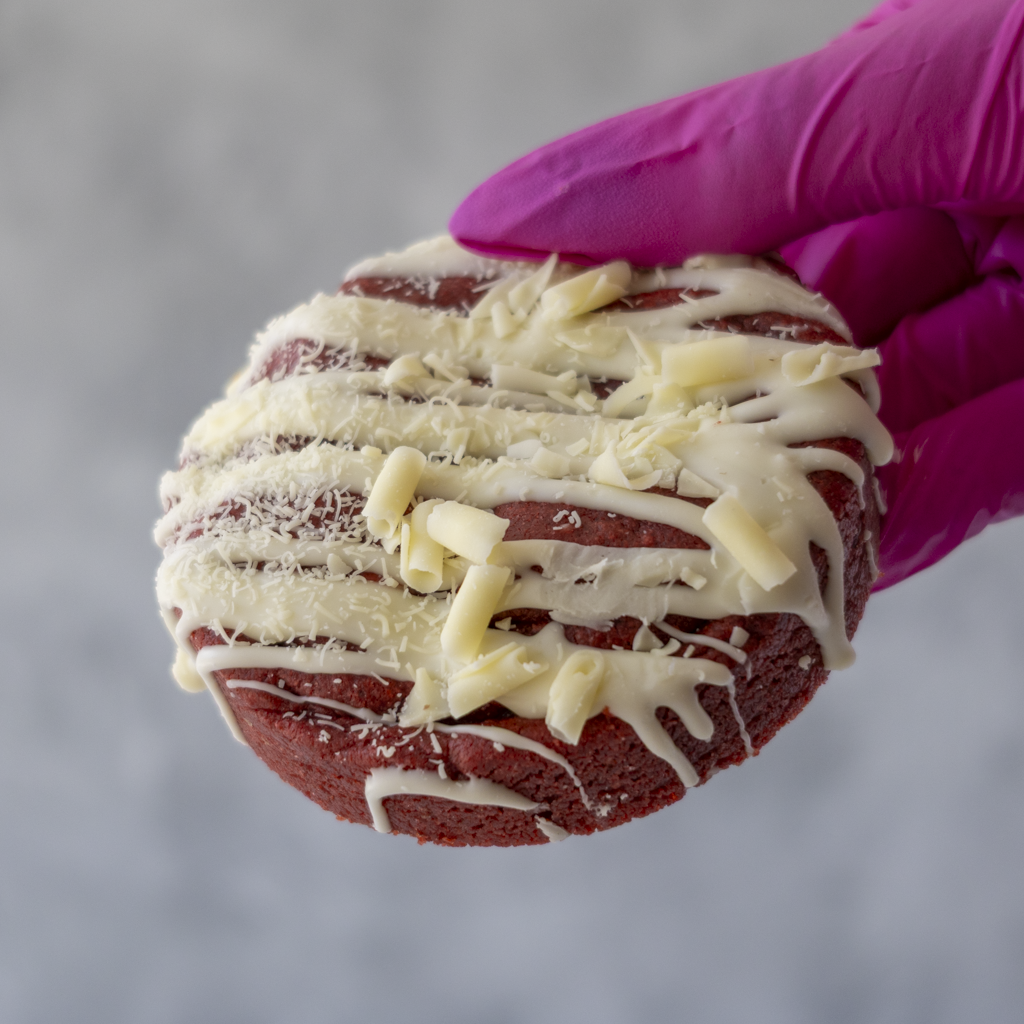 DoughGirl Red Velvet Deluxe Cookie held in pink glove on neutral background