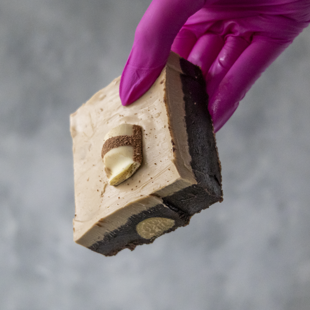 Bueno Brownie Slab with a creamy filling held by a hand wearing a pink glove on a gray background