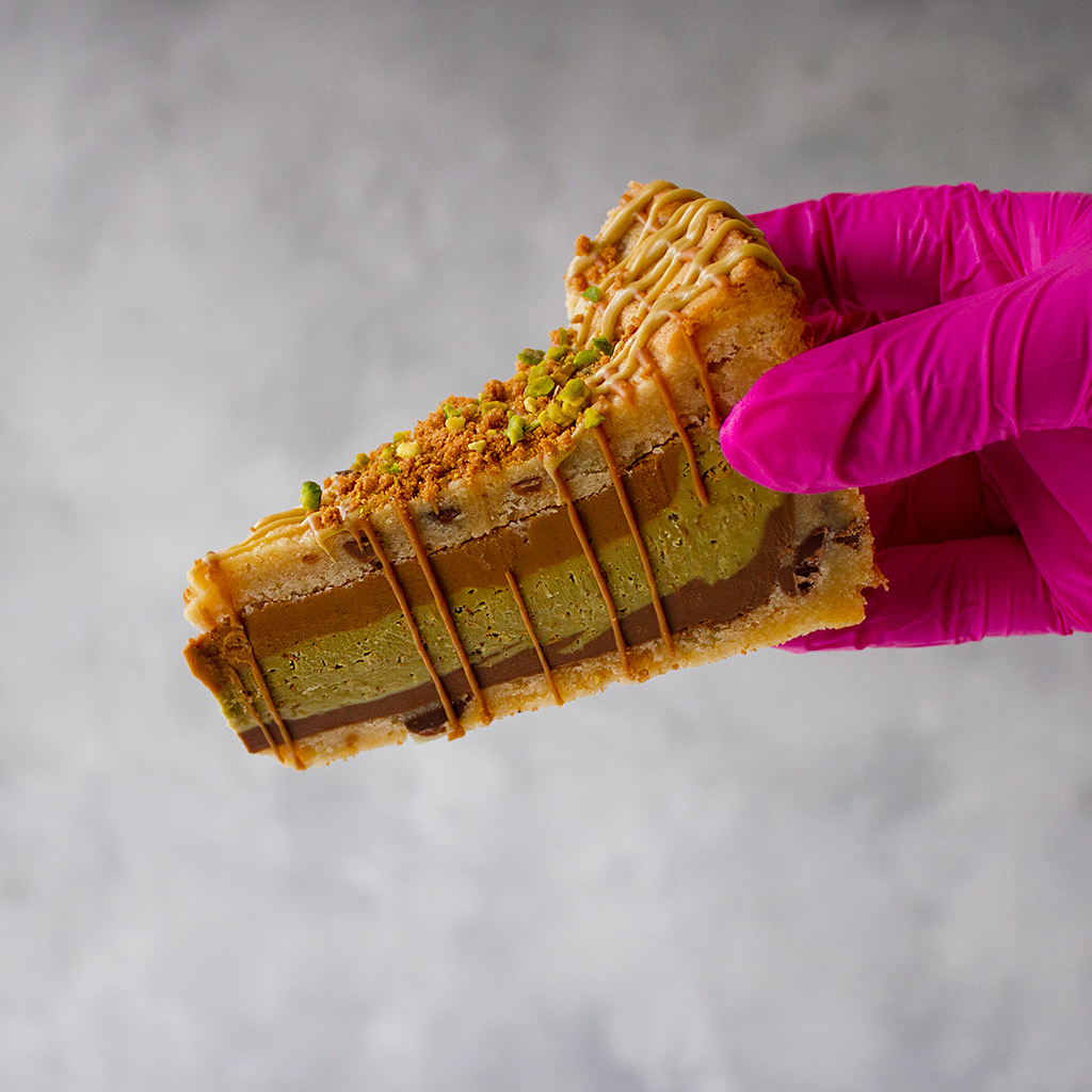 Slice of layered dessert by DoughGirl UK held by a hand in a pink glove against a neutral background