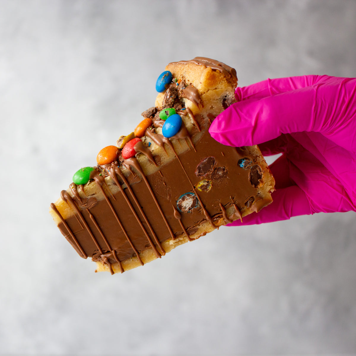 Hand holding a M&M Cookie Pie with colorful candies, ideal for parties or birthday gifts.