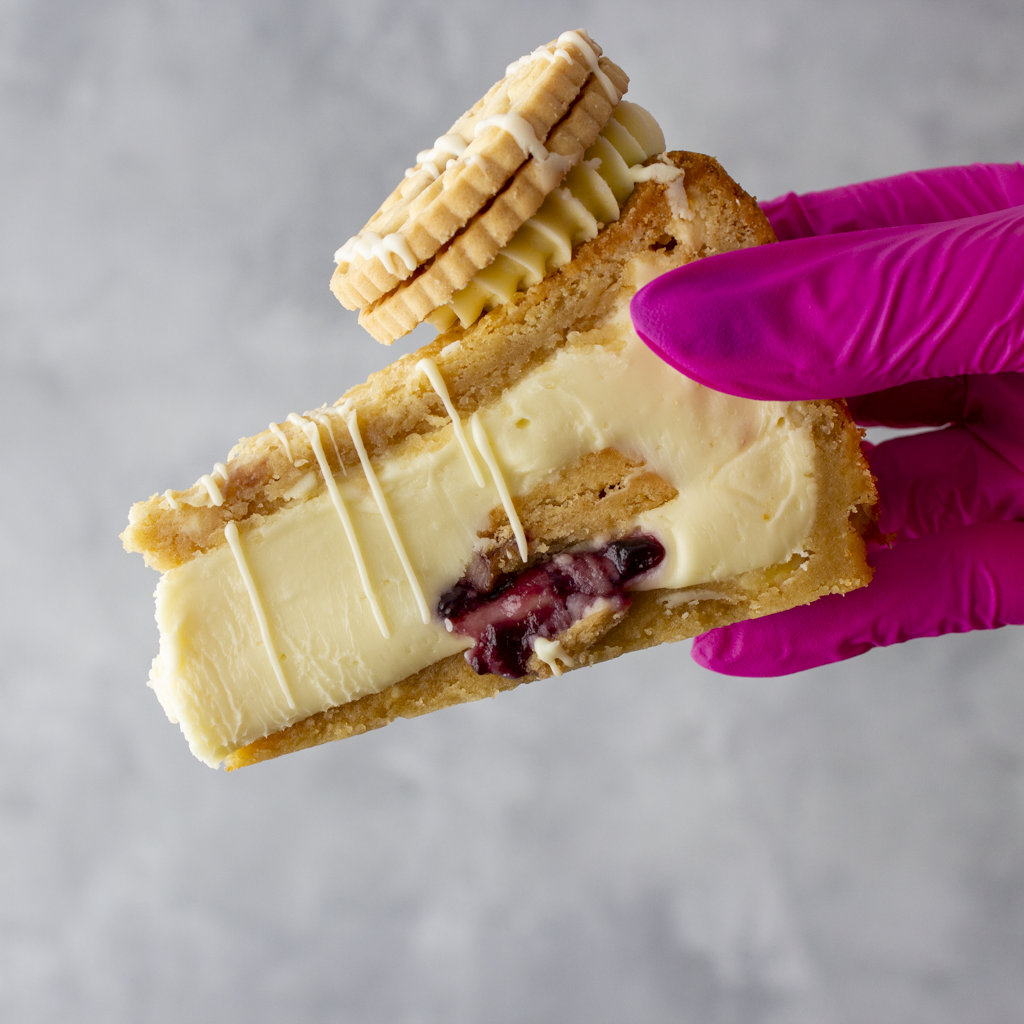 DoughGirl Cookie Pie Slice with Jammie Dodger held in pink glove showing fruity jam centre