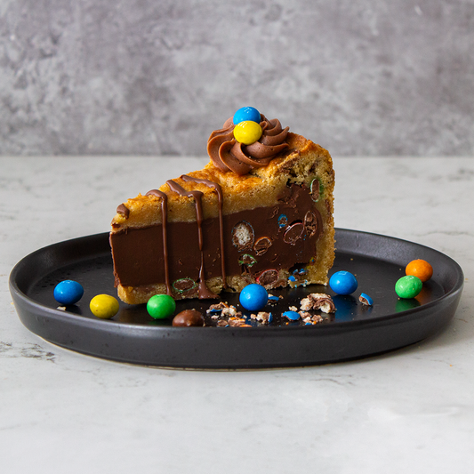 DoughGirl Cookie Pie Slice with M&M’s on a black plate against a grey background