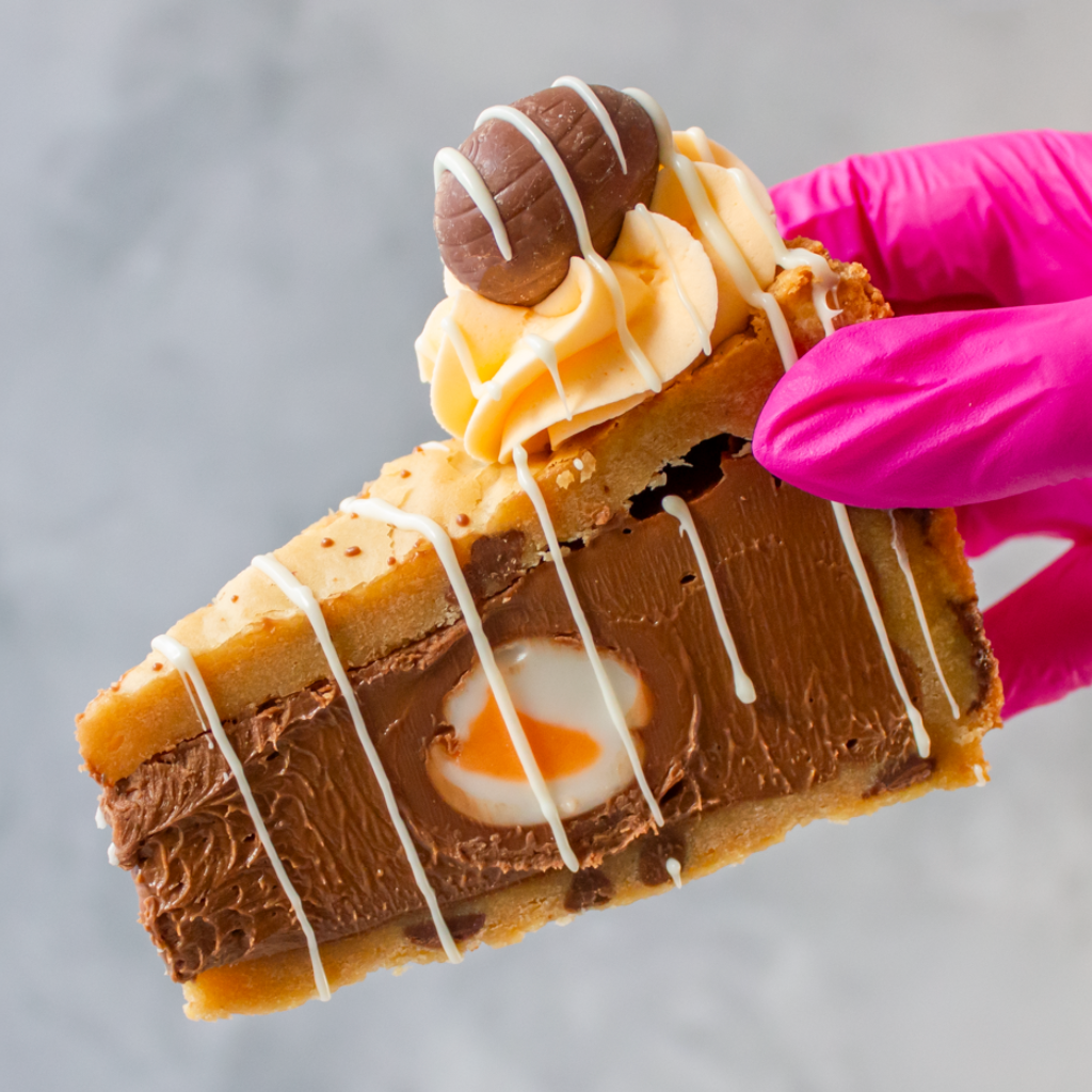 DoughGirl Cookie Pie Slice With Creme Egg hold by a pink gloved hand