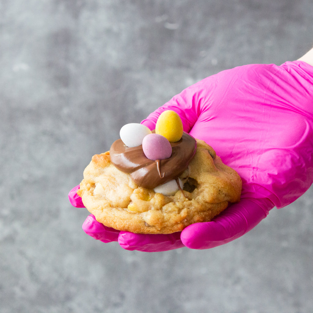 DoughGirl deluxe cookie topped with chocolate and colourful mini egg sweets held by hand