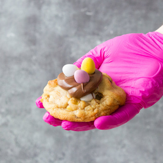 DoughGirl deluxe cookie topped with chocolate and colourful mini egg sweets held by hand