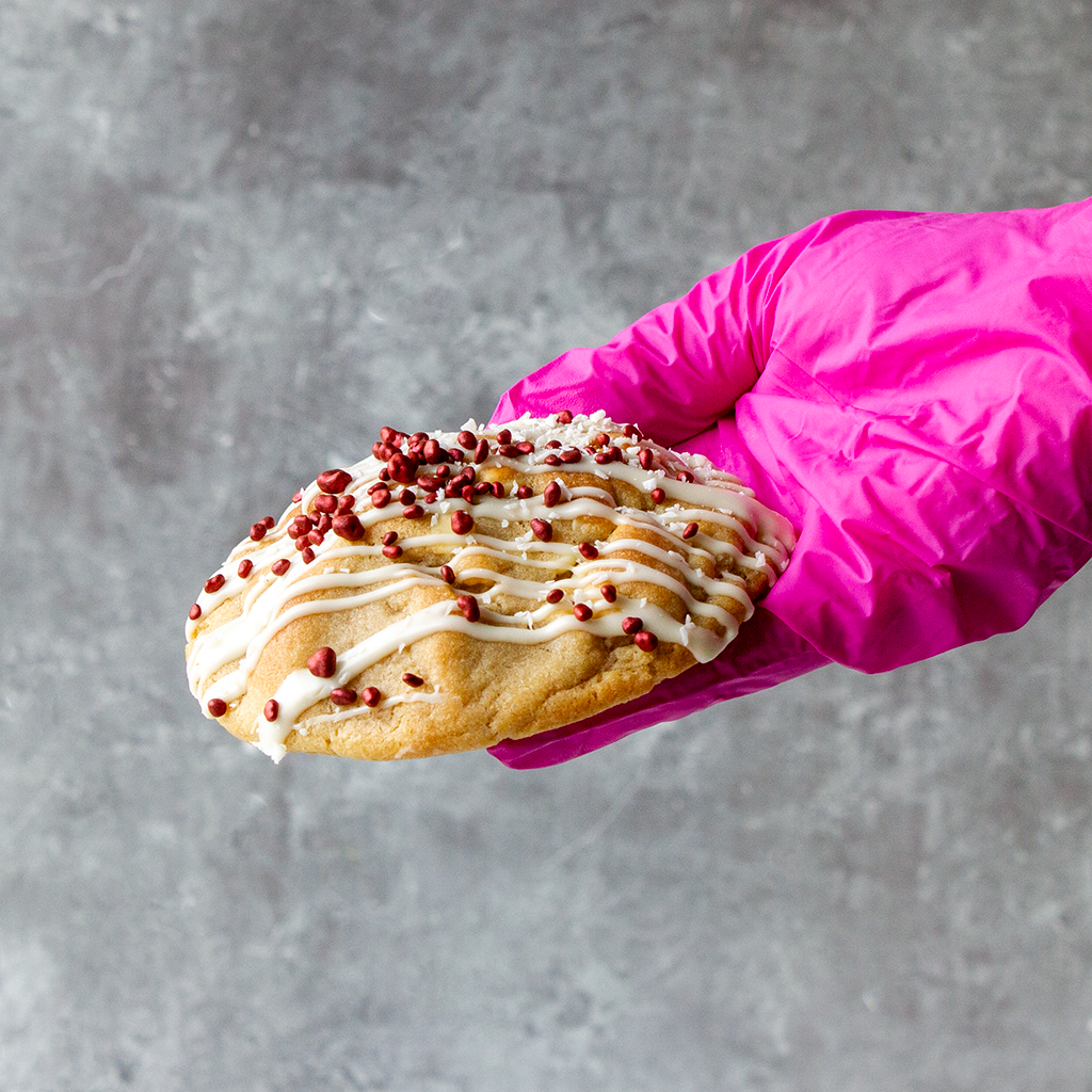 DoughGirl deluxe cookie with white chocolate drizzle and raspberry pieces held by hand