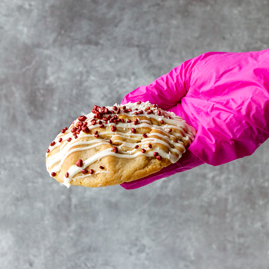 DoughGirl deluxe cookie with white chocolate drizzle and raspberry pieces held by hand