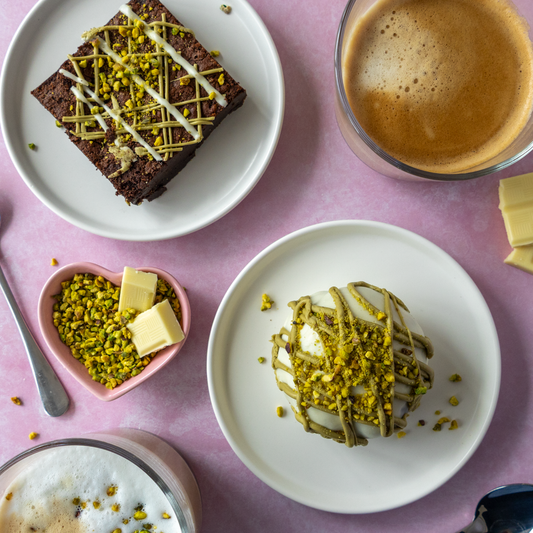DoughGirl’s Pistachio Desserts including a choccy boom bite and a brownie slab, with coffee and other desserts, on a pink surface