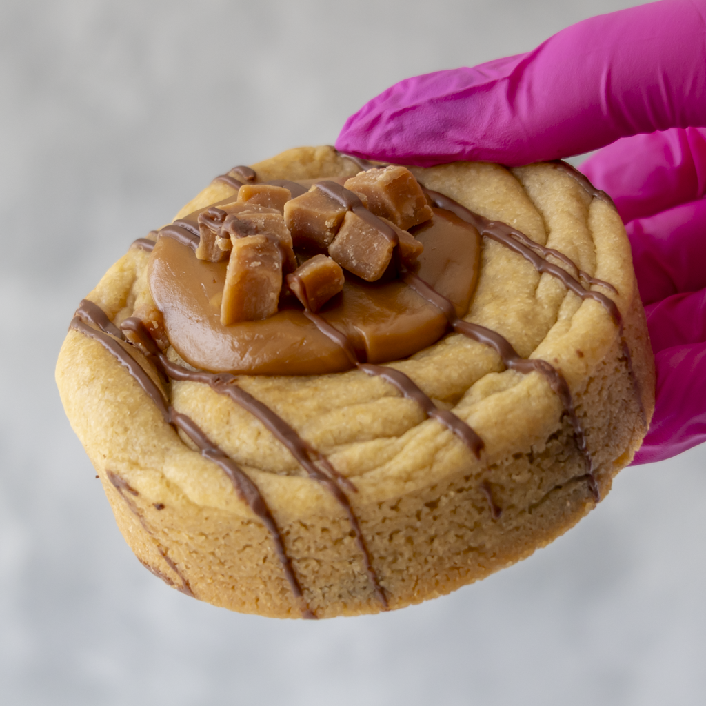 Caramel cookie topped with fudge pieces and chocolate drizzle