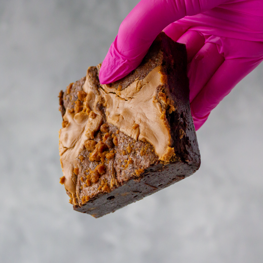 DoughGirl Biscoff Brownie Slab with Lotus Biscoff spread held by a gloved hand against a neutral background