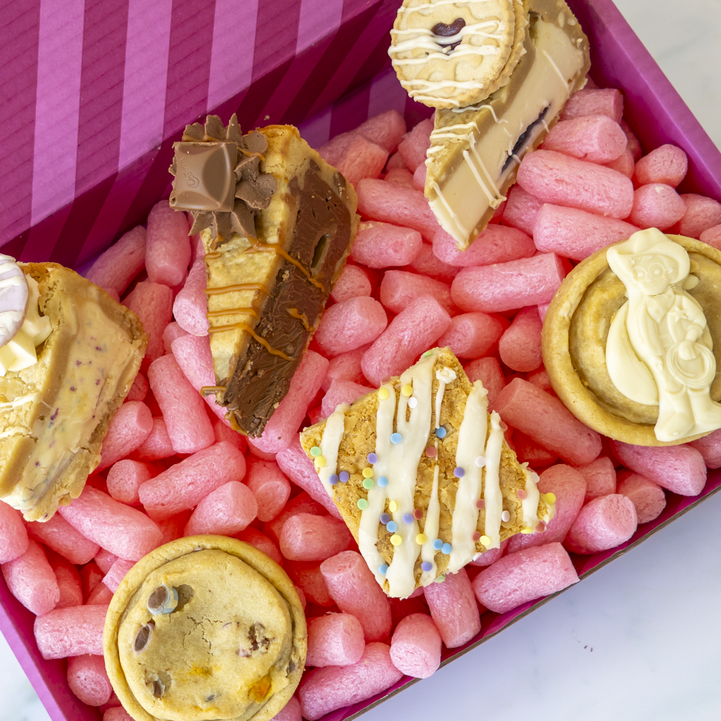 A boxed assortment of assorted cookies, cookie pies and chocolate treats arranged in pink gift box.