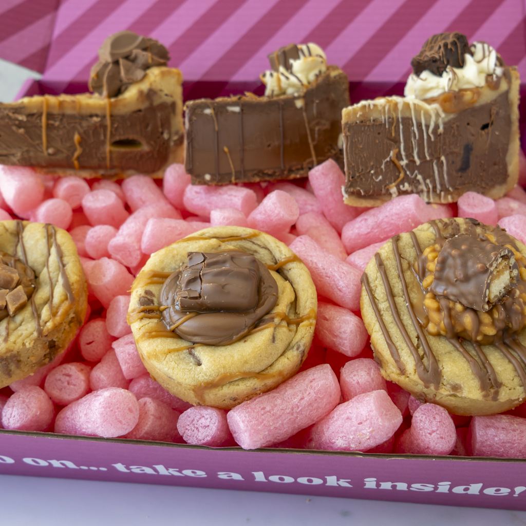 A close-up of assorted chocolate-dipped cookies and cookie pie slices arranged in pink cookie box.