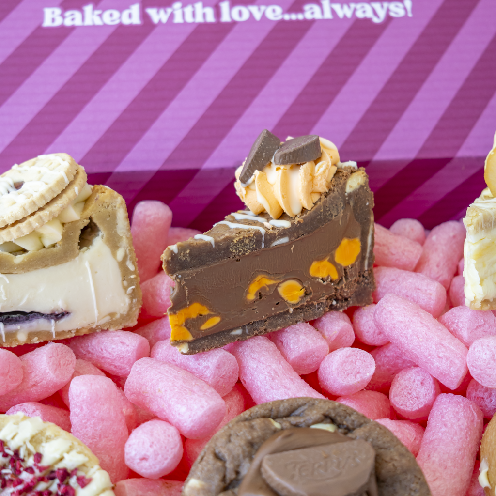 A close-up of assorted gourmet chocolates and sweets arranged on pink box with diagonal stripes and the text 'Baked with love...always!"
