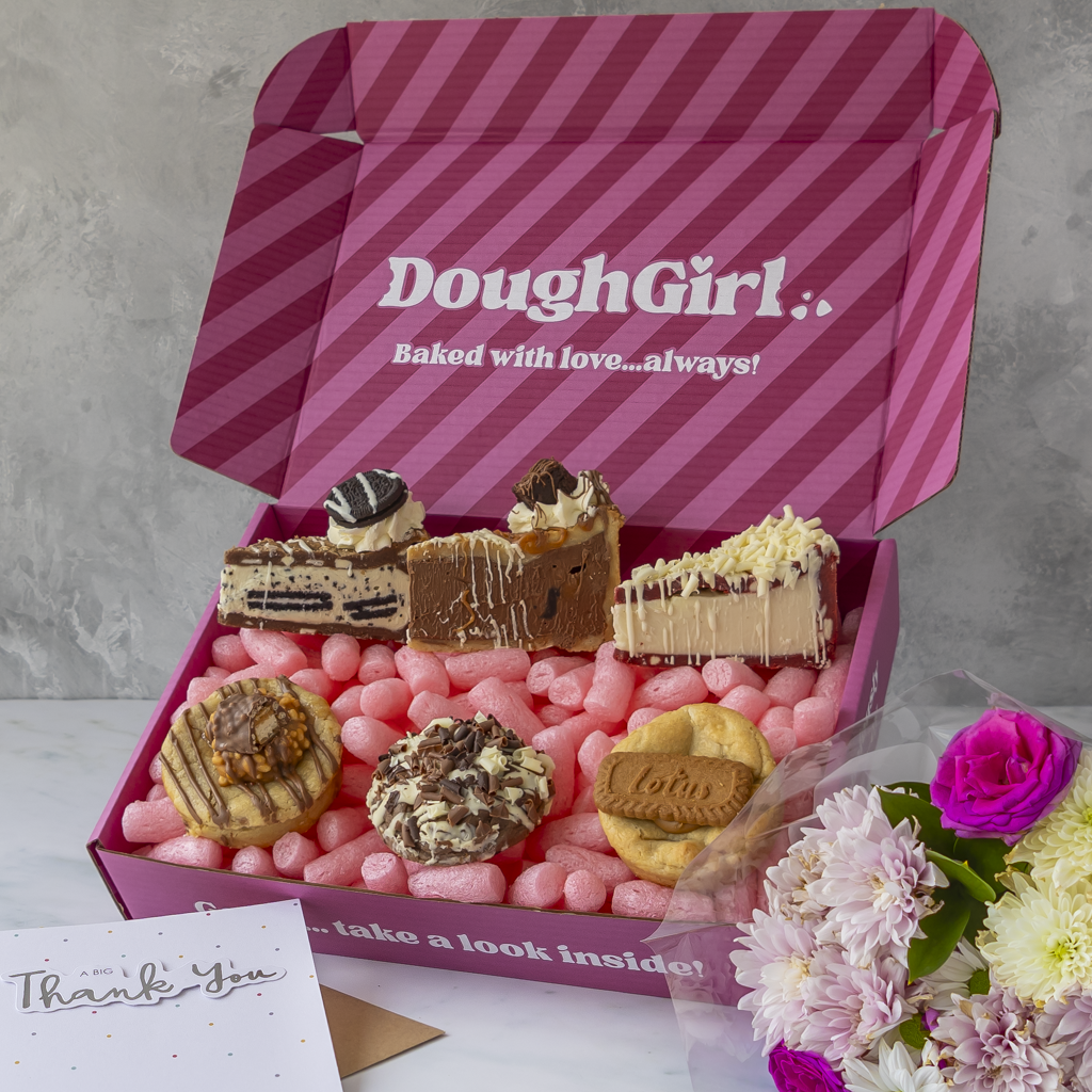 An open pink striped gift box branded DoughGirl with flowers and a thank-you card against a marble background.