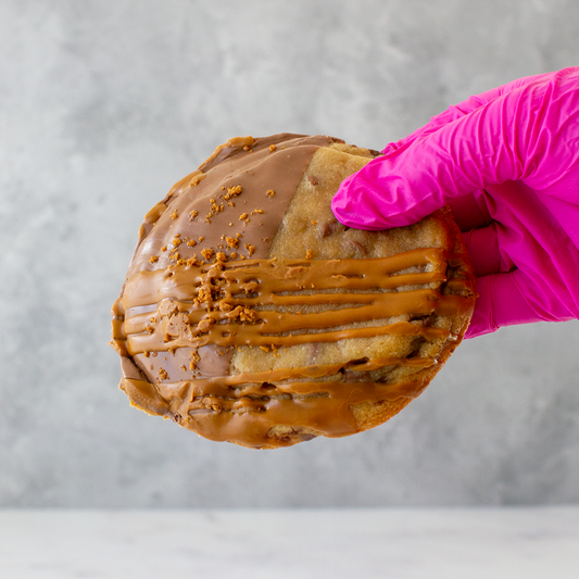 Hand wearing a pink glove holding a Biscella Deluxe Cookie with chocolate icing against a gray background