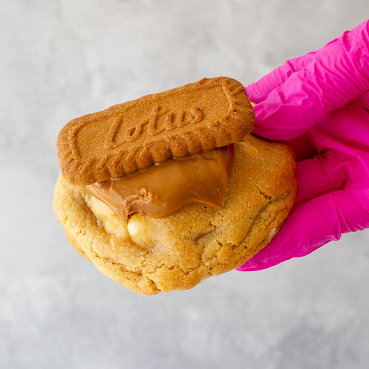 Biscoff Deluxe Cookie with a Biscoff spread held by a hand wearing a pink glove on a light gray background