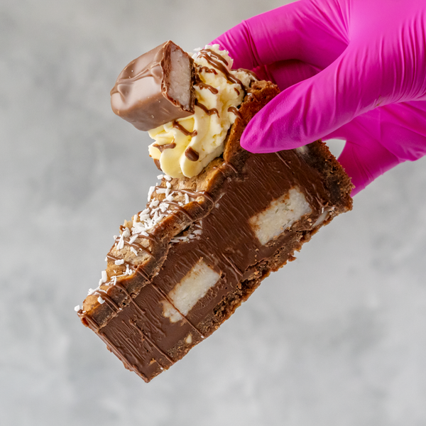 Bounty Cookie Pie Slice with a person wearing a pink glove holding it against a neutral background