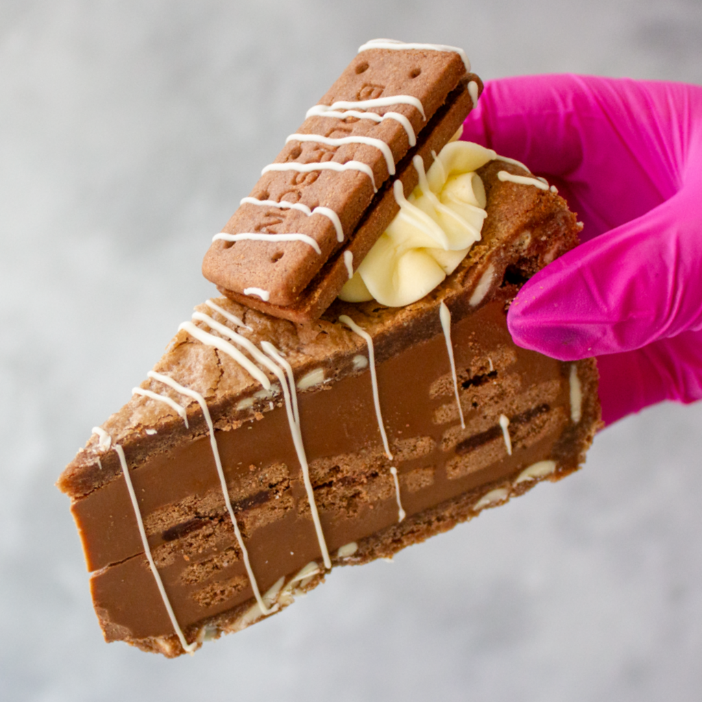 DoughGirl Bourbon Biscuit Cookie Pie Slice with white drizzle held by a hand in a pink glove against a gray background