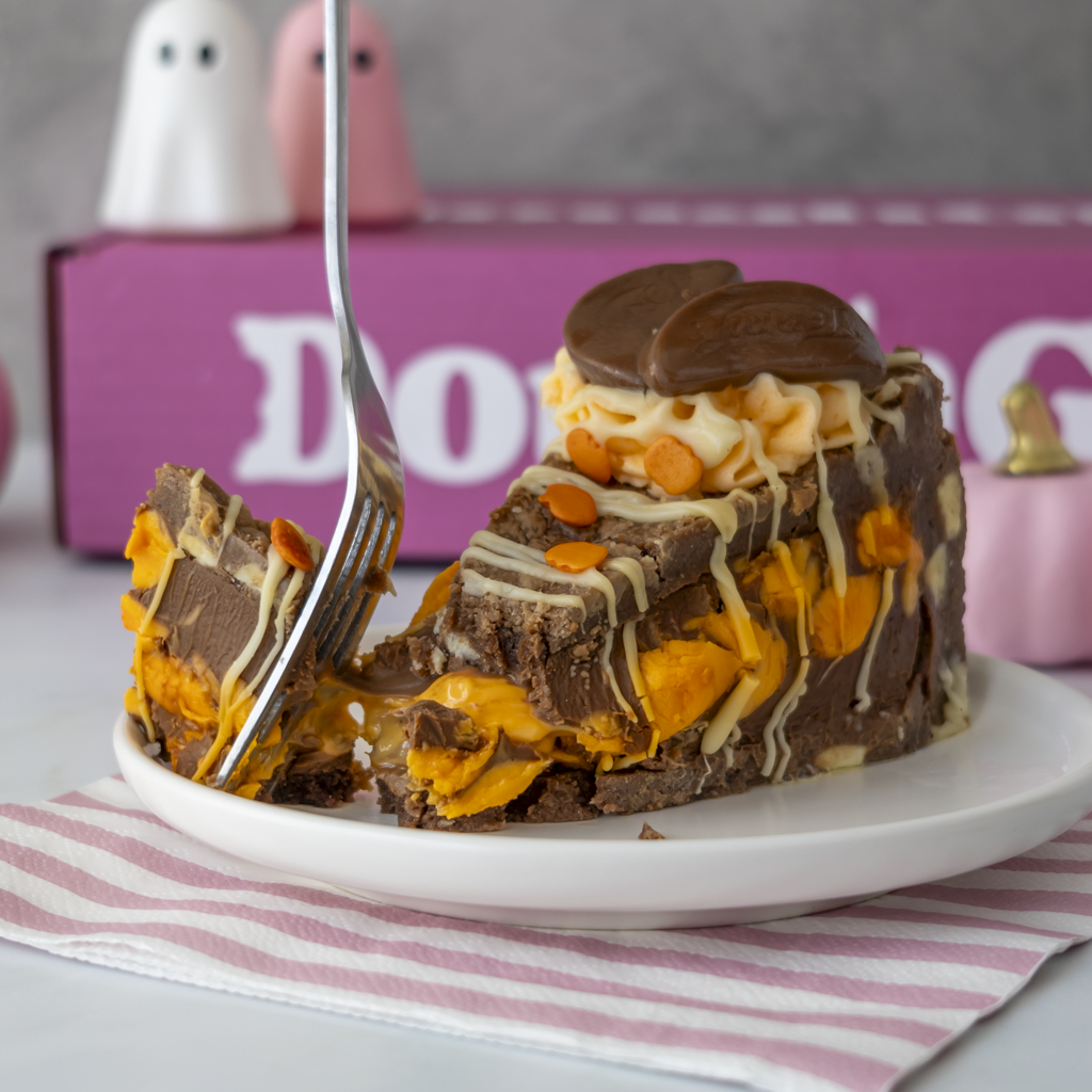 A slice of Chocolate & Orange Fright Cookie Pie dessert on a white plate with a fork, set against a pink decorative box and small ghost figurines.
