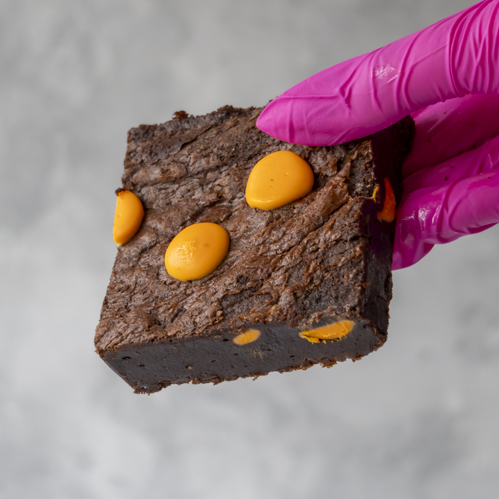 DoughGirl Chocolate Orange Brownie Slab with velvety chocolate held by a gloved hand on a gray background