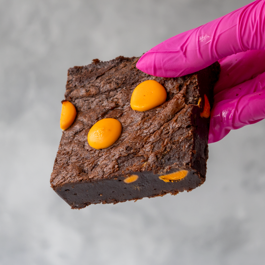 DoughGirl Chocolate Orange Brownie Slab with velvety chocolate held by a gloved hand on a gray background