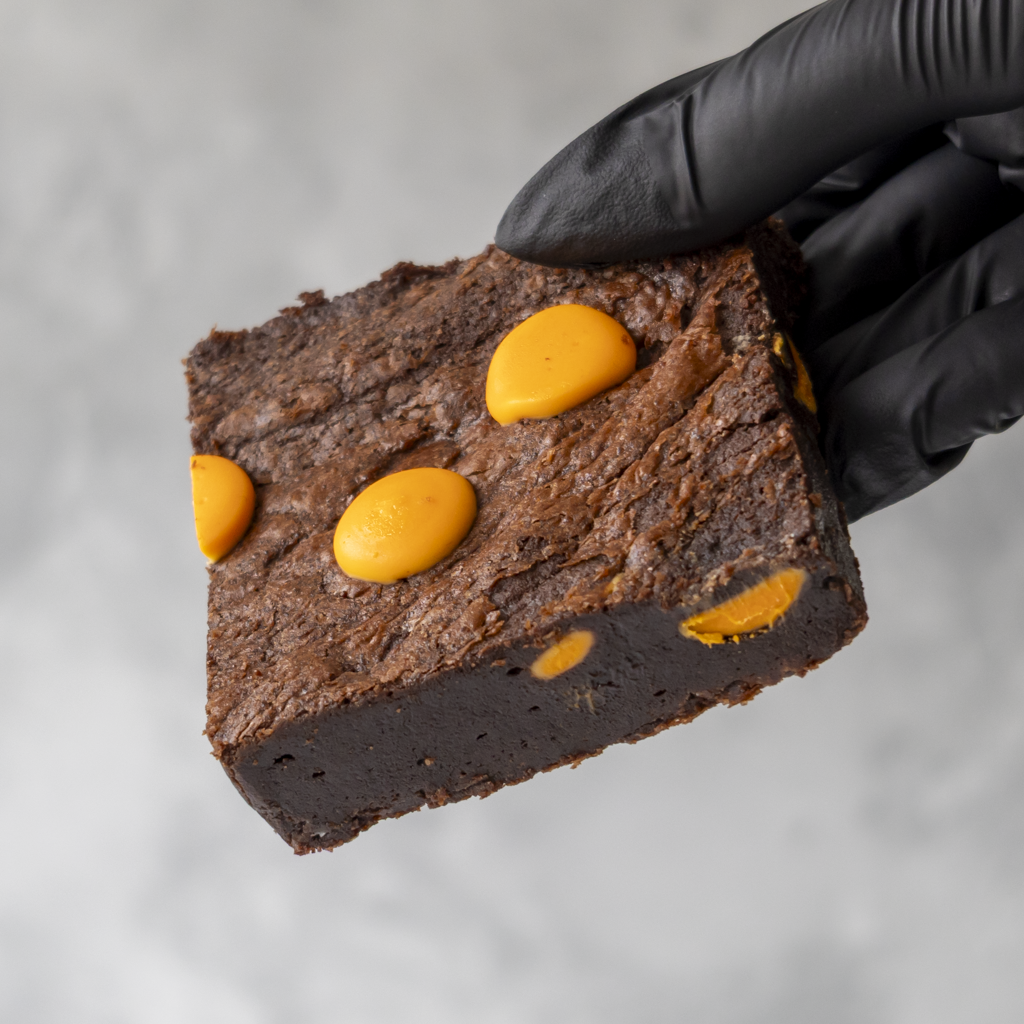 Chocolate Orange Brownie Slab with orange sweet held by a gloved hand against a neutral background