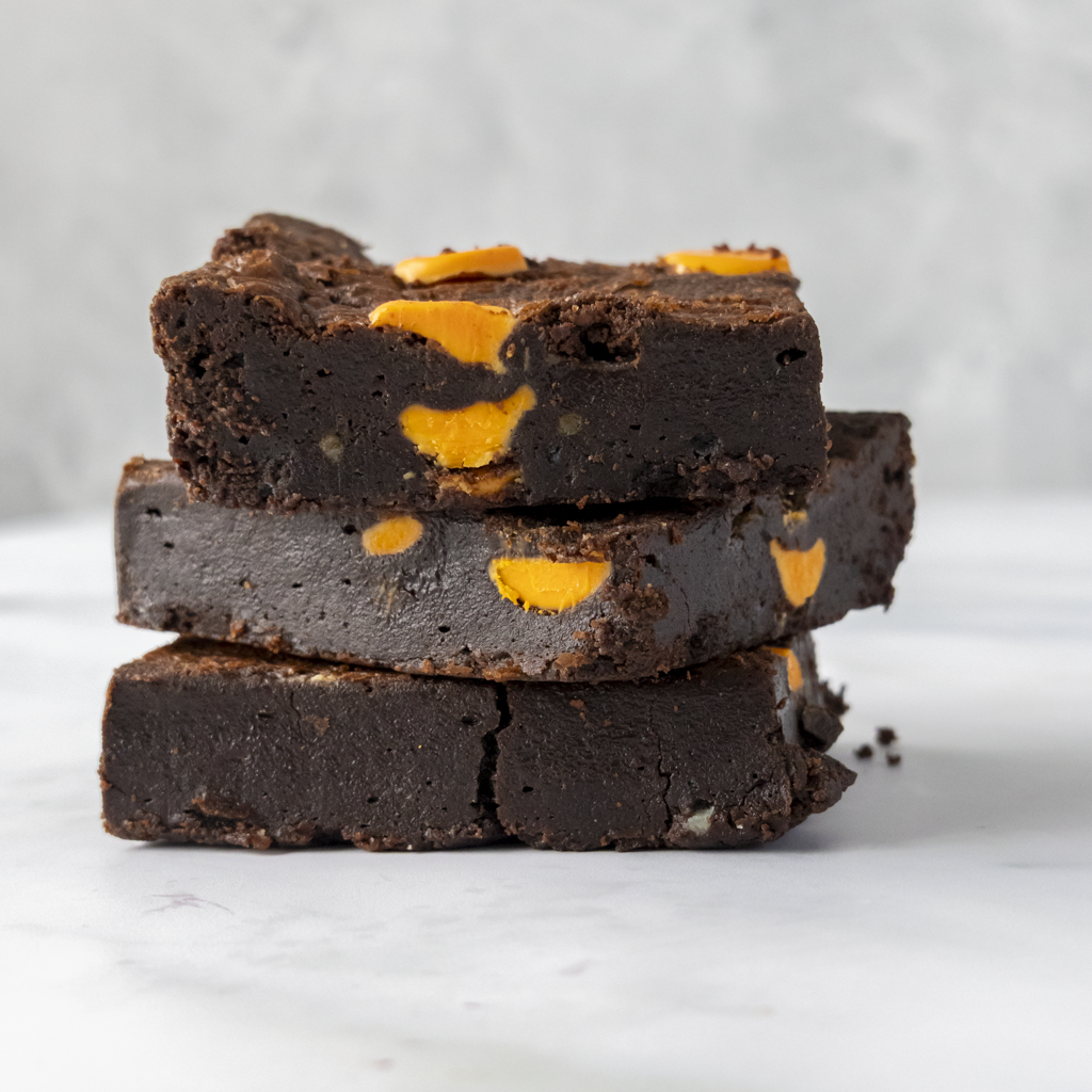 Stack of chocolate brownies with orange sweet pieces on a light gray background