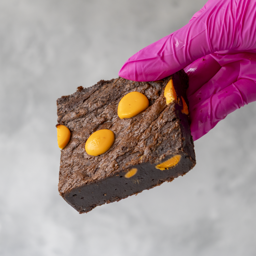 Brownie with Chocolate Orange pieces held by a hand in a pink glove.