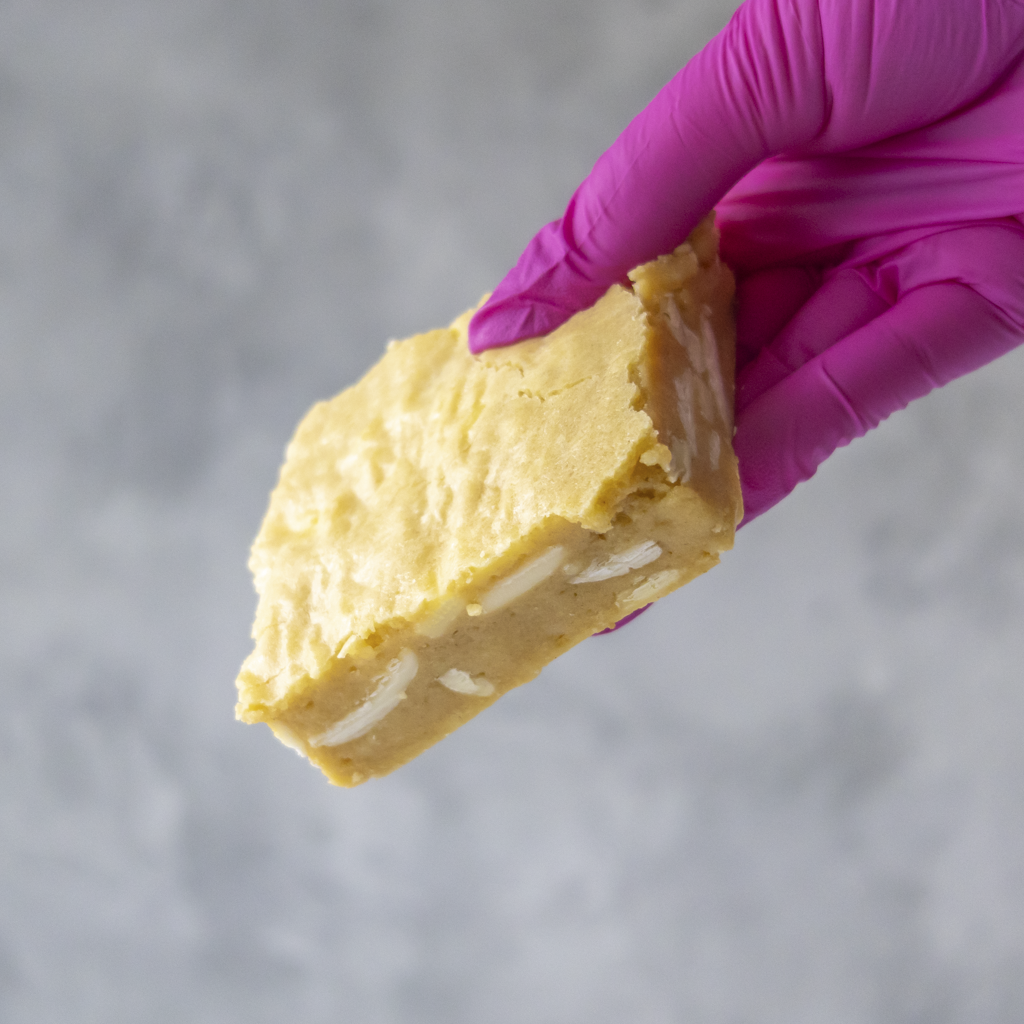 Classic Brookie Slab by DoughGirl UK with white filling held by a hand in a pink glove against a gray background