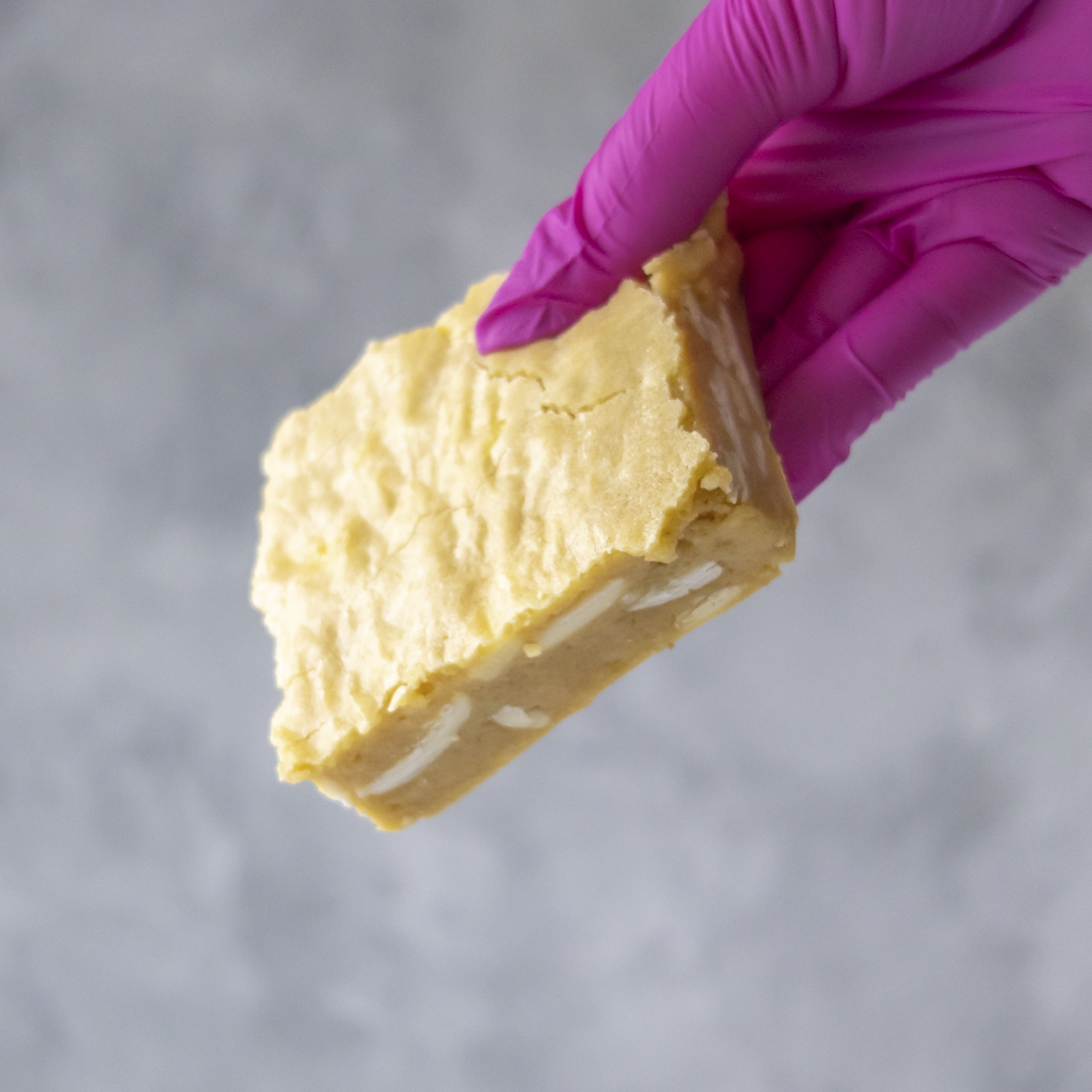Hand wearing a pink glove holding a Classic Brookie Slab with white cream on a gray background