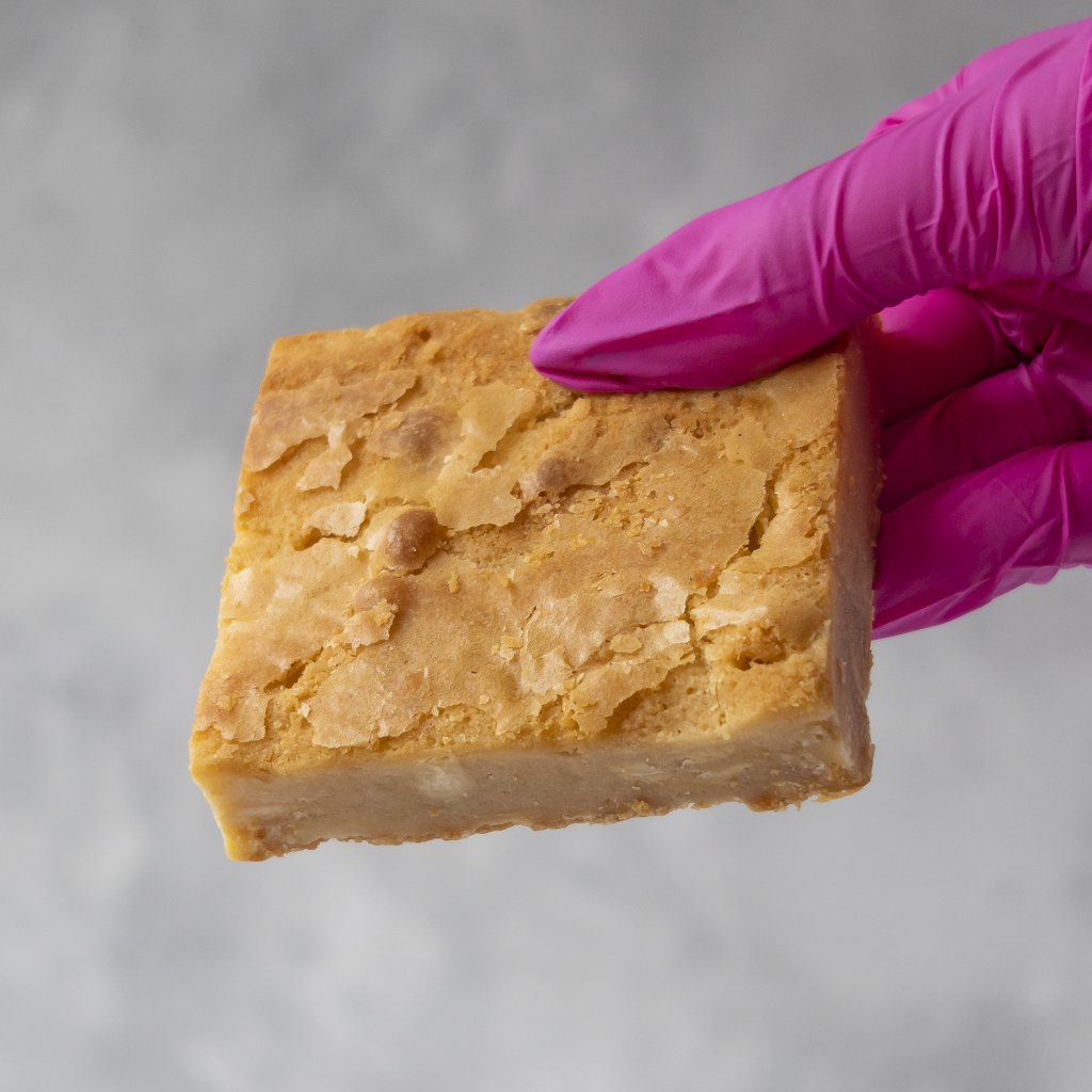 DoughGirl Classic Blondie Slab held in pink glove with golden top and white chocolate chunks