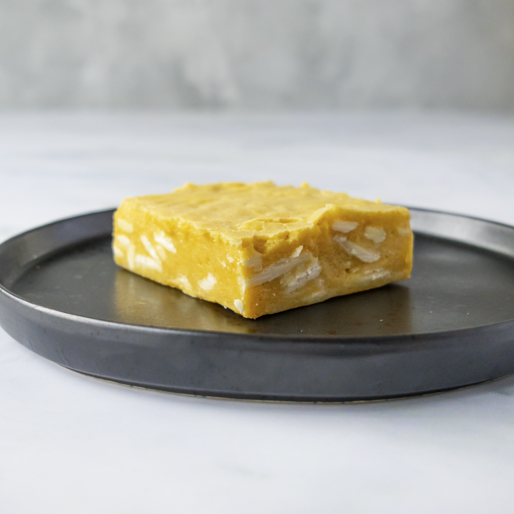Square dessert slab with creamy white chocolate chunks on a black plate with a gray background