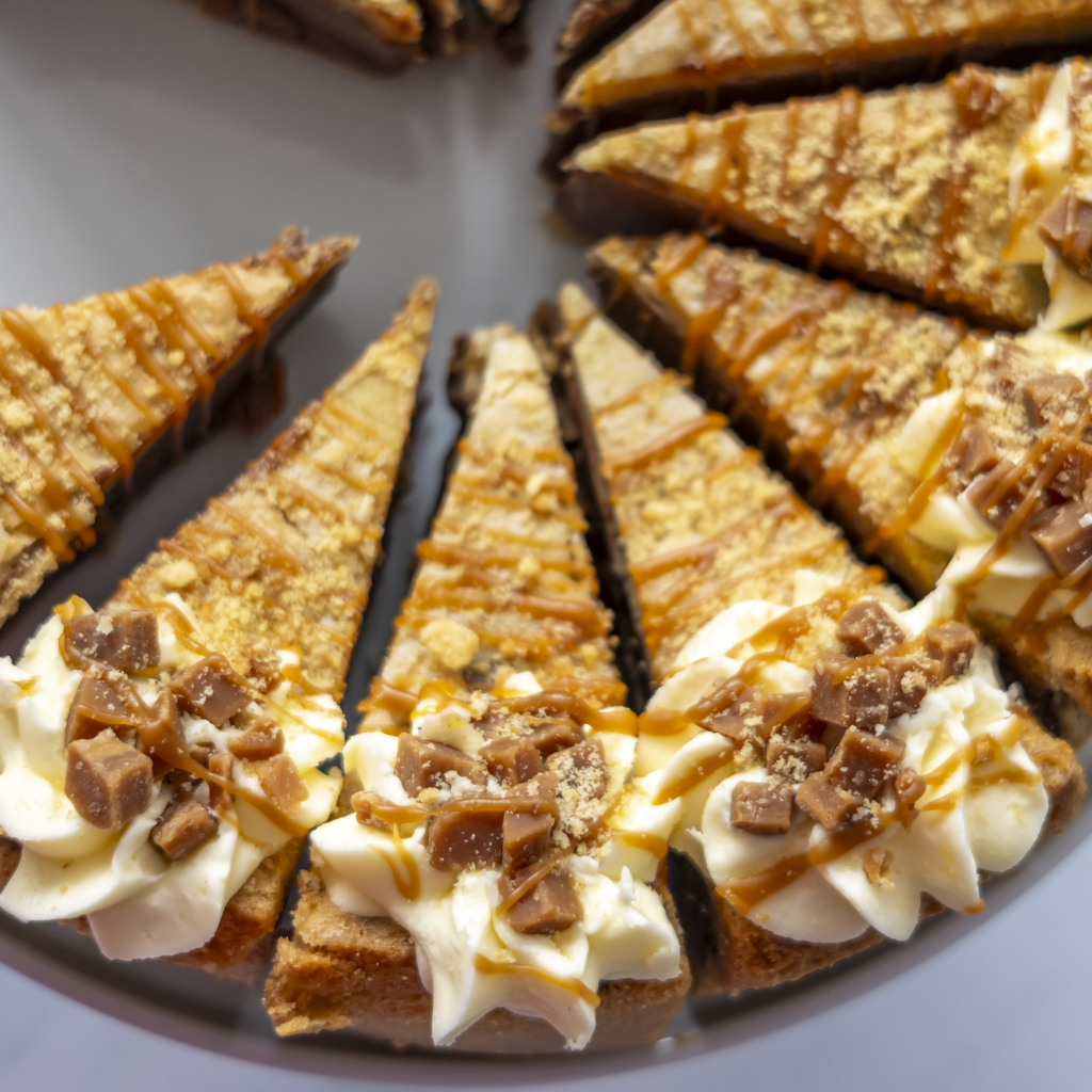 Close-up of several triangular slices of a Banoffee Cookie Pie Slice on a plate, topped with whipped cream, chopped chocolate pieces, and caramel drizzle.