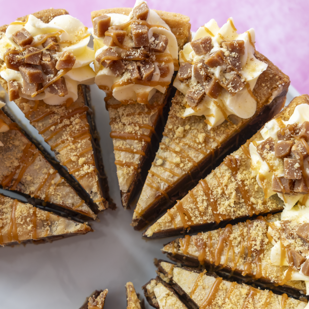 Slices of a Banoffee Cookie Pie arranged in a circle on a white plate, with whipped cream, cookie crumbs, and chocolate chunks on top, set against a soft pink background.