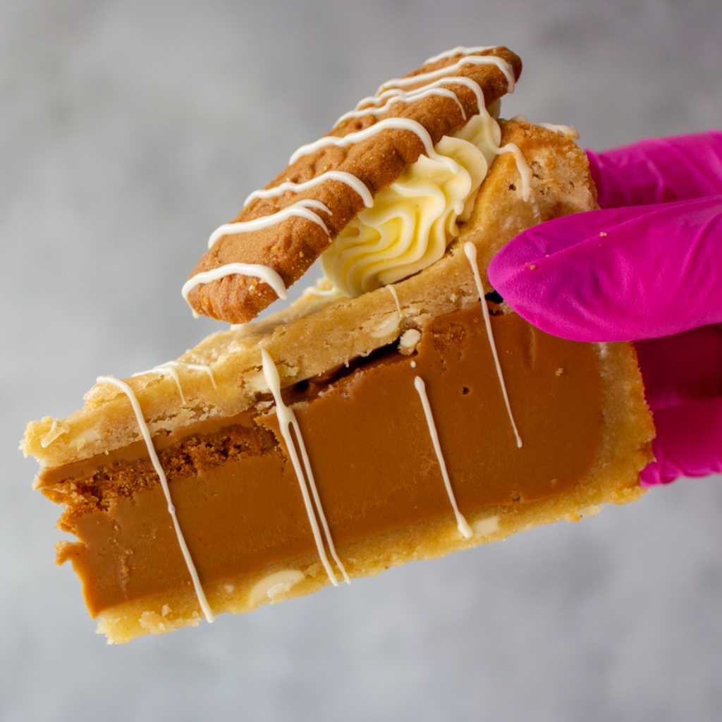 Biscoff Cookie Pie with white drizzle held by a gloved hand against a neutral background