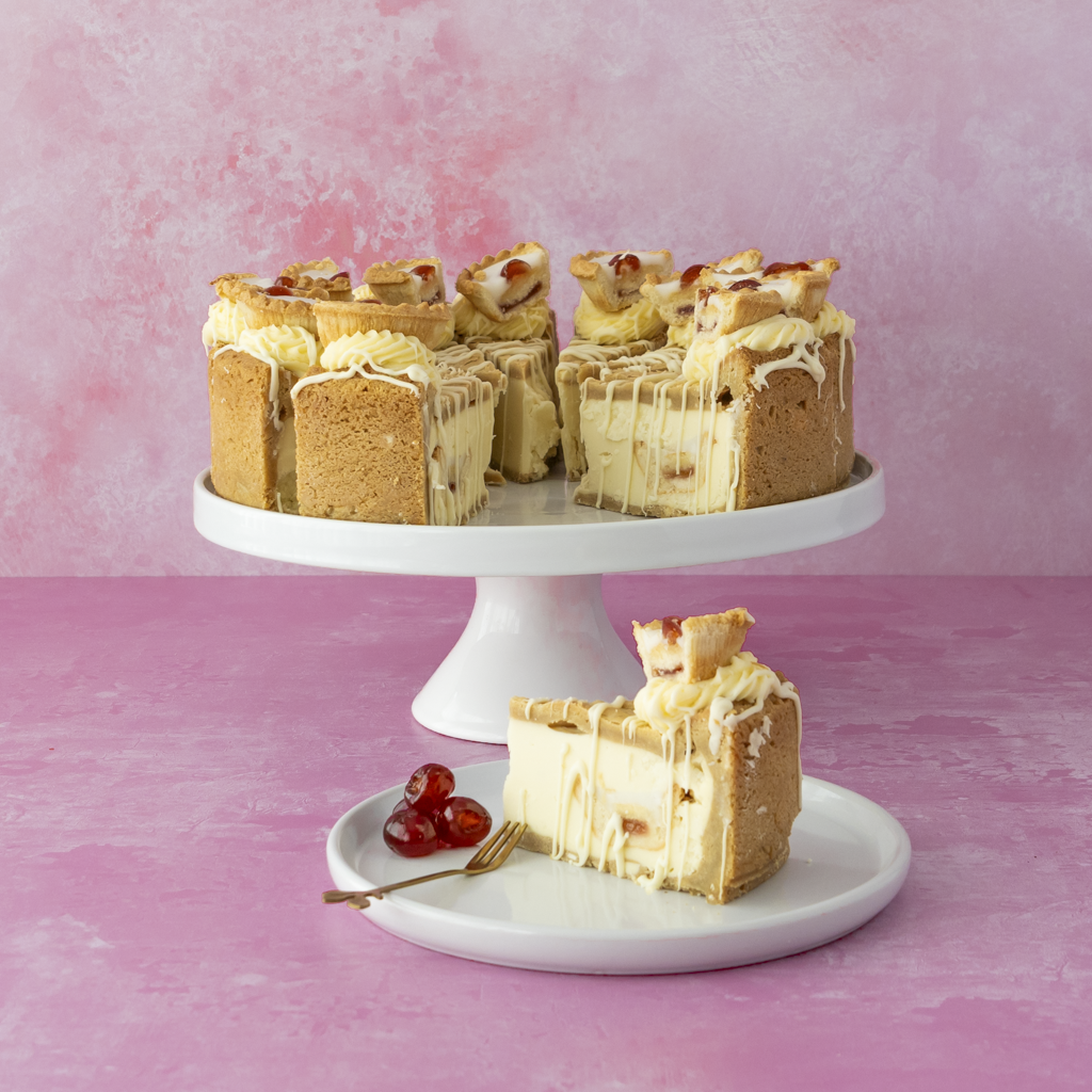 Full 12-Slice Cherry Bakewell Cookie Pie by DoughGirl UK on a white stand with a slice on a plate against a pink background