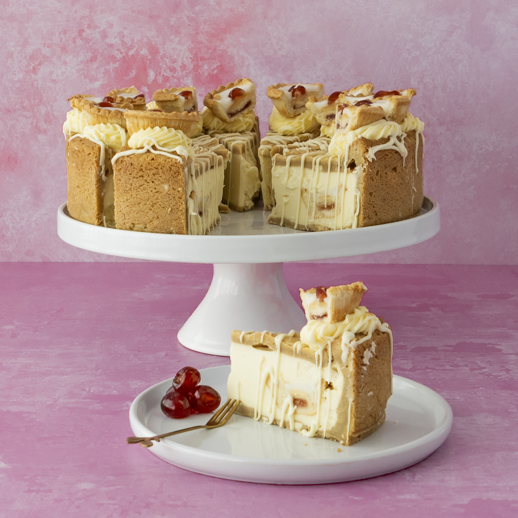 Full 12-Slice Cherry Bakewell Cookie Pie on a white stand with a slice on a plate and some cherries against a pink background
