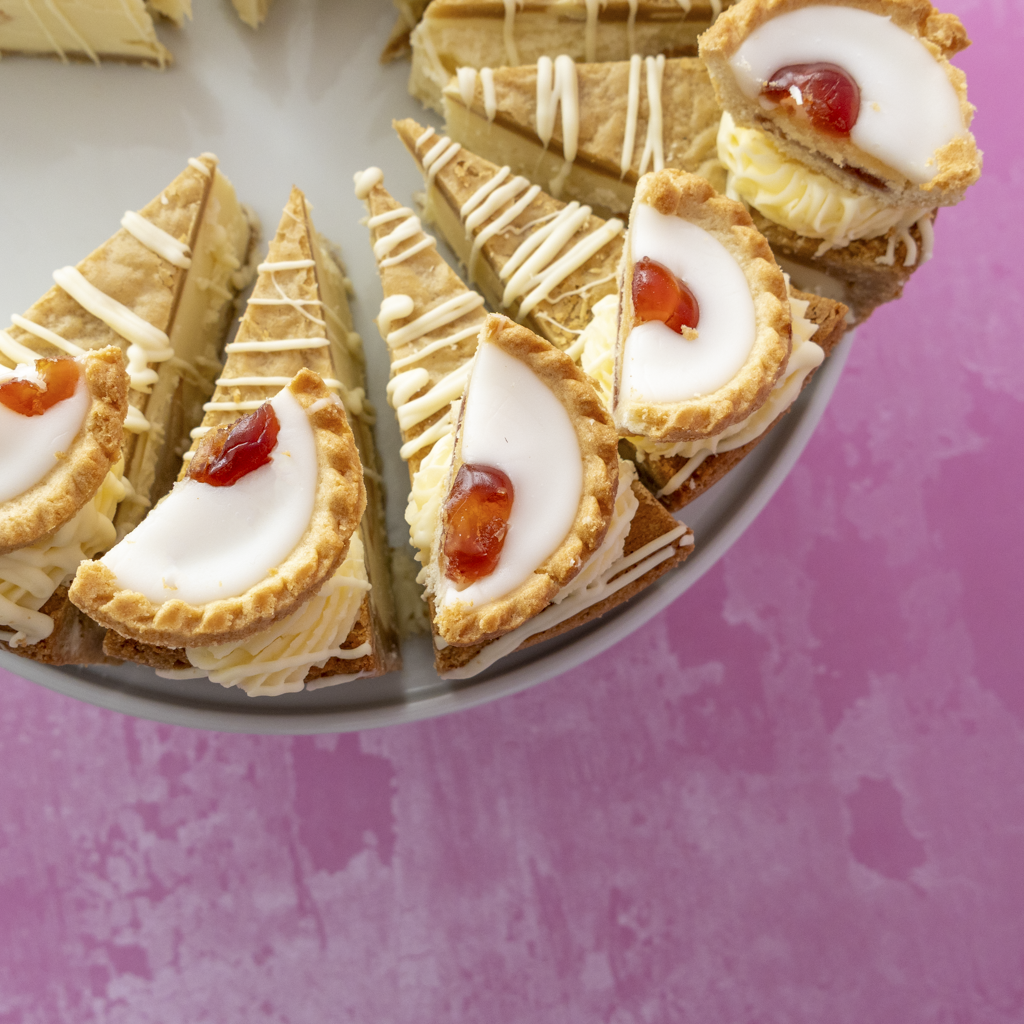 Slices Cherry Bakewell Cookie Pie with cream and jam on a plate against a pink background