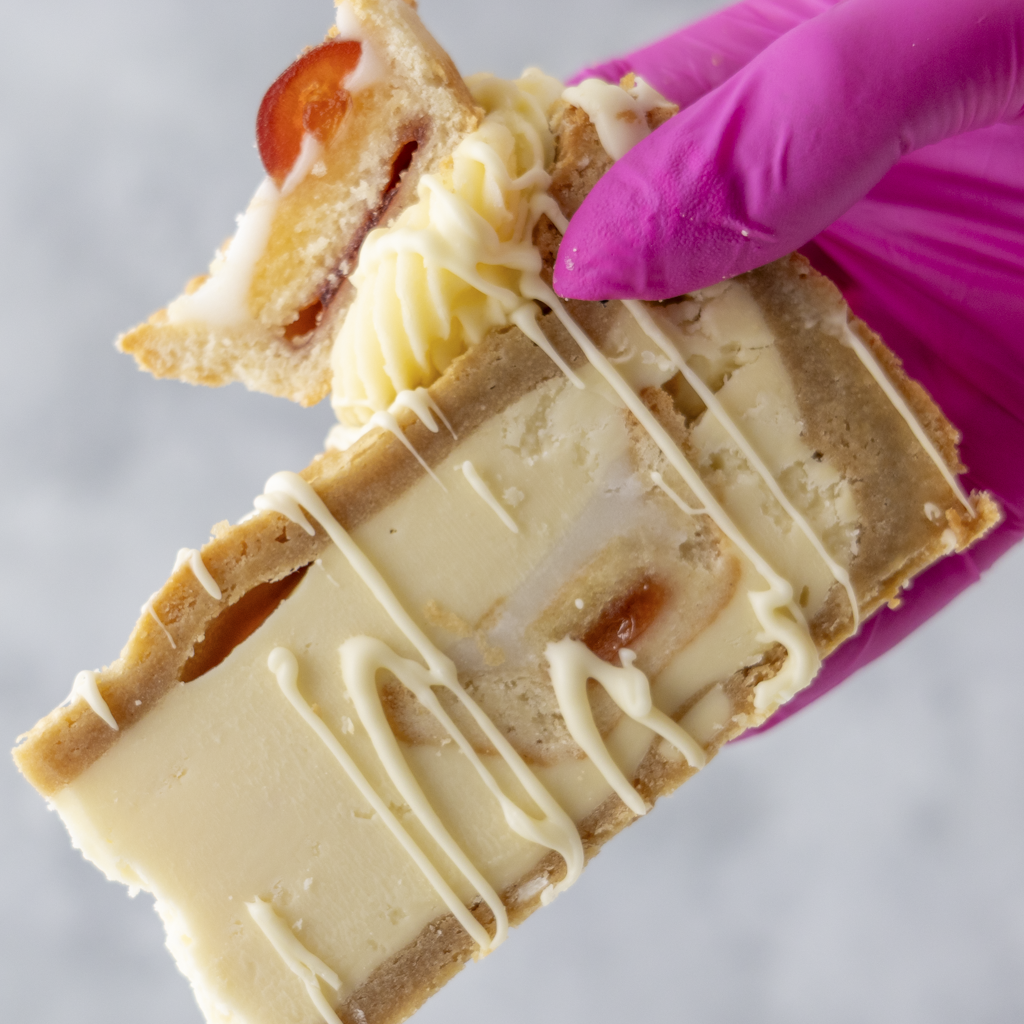 Hand holding a slice of white chocolate-dipped cookie with a pink glove on a gray background