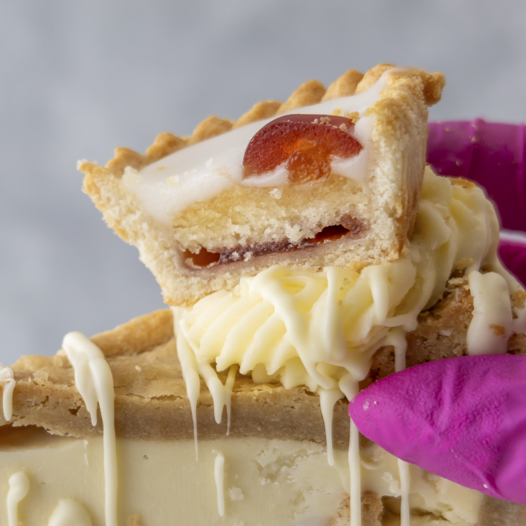 Close-up of a Cherry Bakewell Cookie Pie with white frosting and a pink glove holding it.