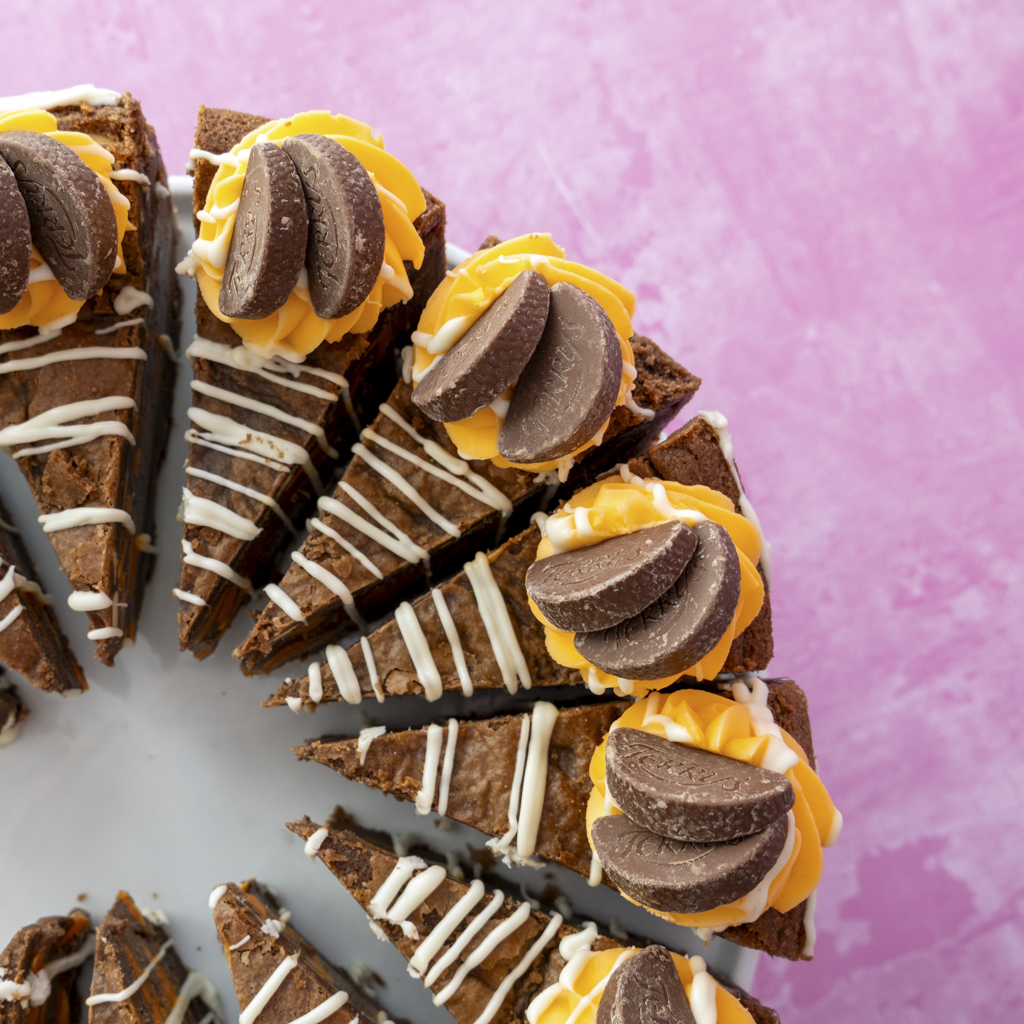 Chocolate cake with orange frosting and cookie pieces on a pink background
