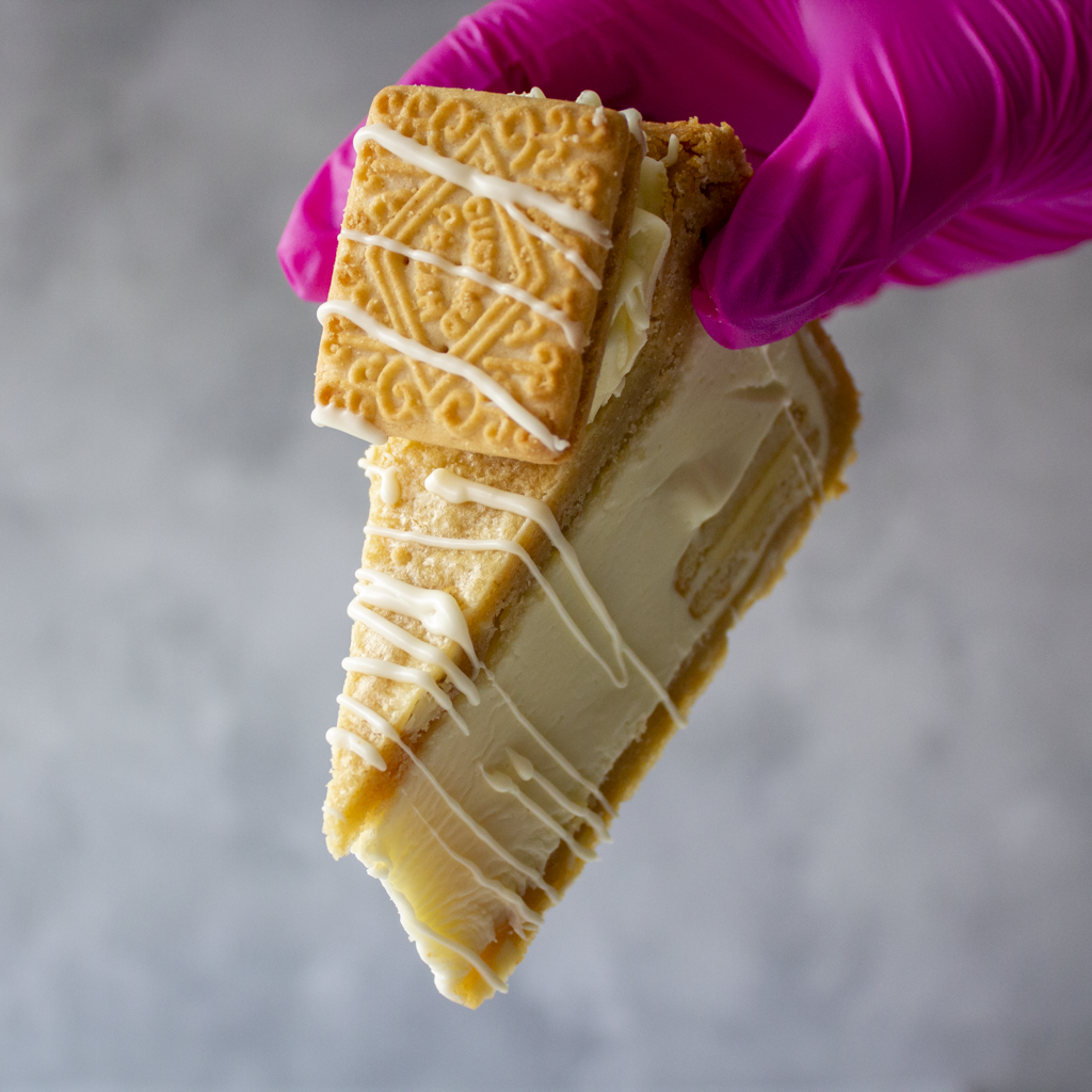 DoughGirl Custard Cream Cookie Pie Slice held in pink glove with biscuit and white chocolate drizzle