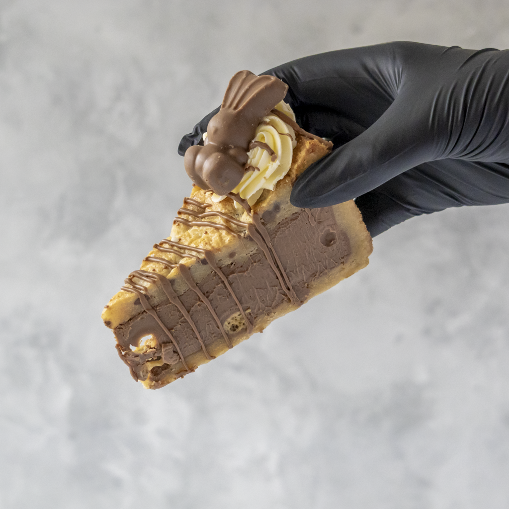 Hand holding a Limited Edition Malteser Bunny Cookie Pie with chocolate bunny and cream details against a gray background
