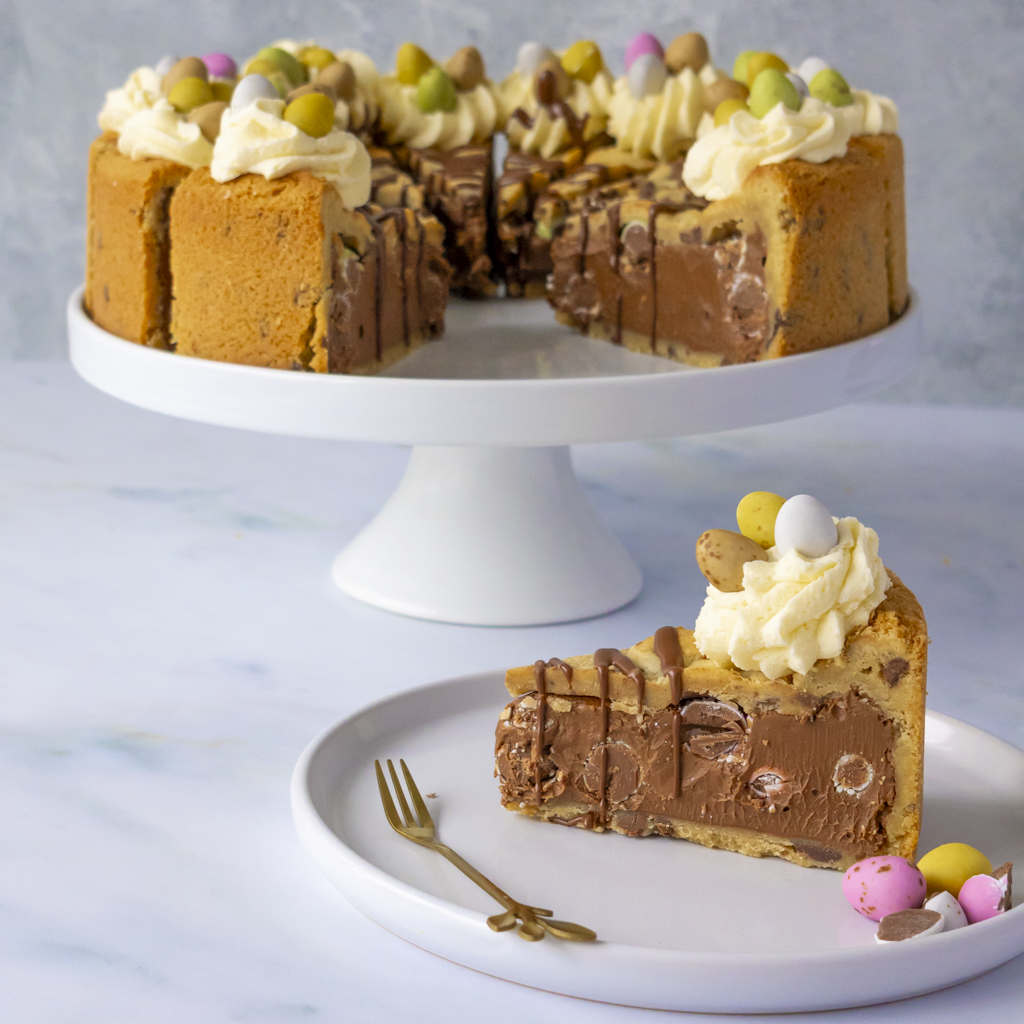 12-Slice Mini Egg Cookie Pie by DoughGirl UK  with a slice on a plate and a whole cake on a white stand.