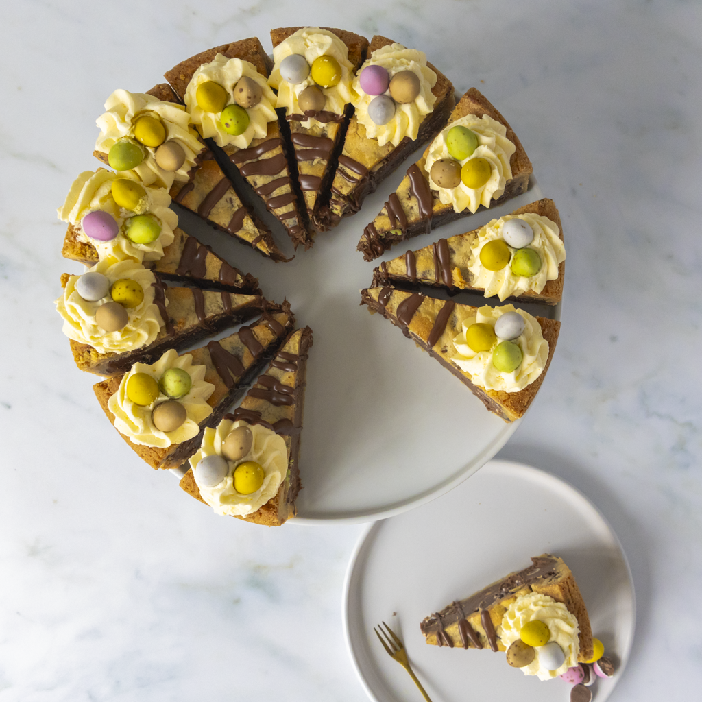 Decorative Easter Egg cake with a slice removed, showing colorful Mini Eggg Chocolate sweets on a marble surface.