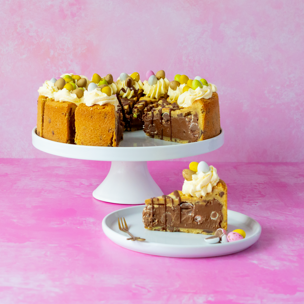 DoughGirl Mini Egg Cookie Pie with a slice on a white plate against a pink background