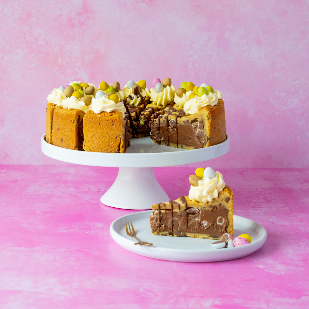 Chocolate cake with white frosting and colorful mini egg candies on a pink background
