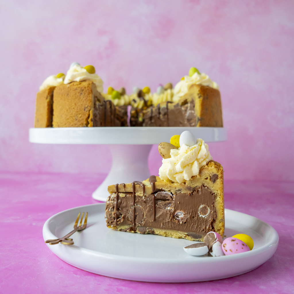 Slice of layered cookie pie with whipped cream and Easter Mini Eggs on a white plate against a pink background